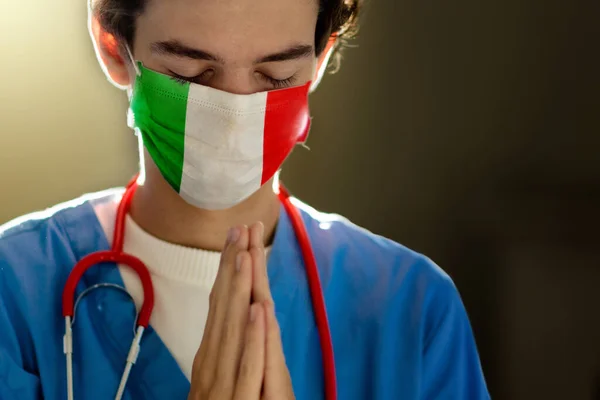Doctor in face mask praying for Italy. Medical staff in hospital chapel or church during coronavirus outbreak. Virus pandemic. People pray. Nurse saying a prayer for sick Italian patient.