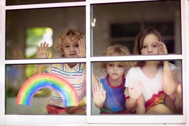 Coronavirus quarantine. Stay home. Kids sitting at window. Children drawing rainbow sign of hope. Boy and girl during corona virus lockdown. Child and pet. Family isolation indoors. Disease prevention clipart