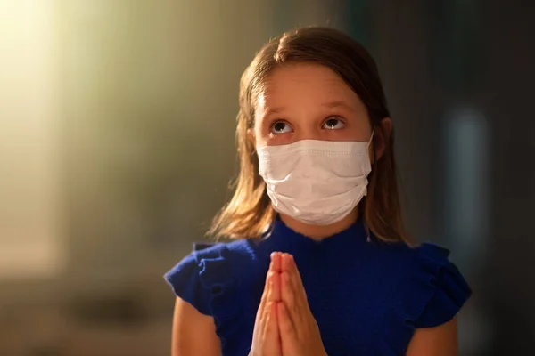 Pray for the sick. Child in face mask praying. Little girl in hospital chapel or church during coronavirus outbreak. Virus pandemic. Kids worship. Children say a prayer for sick patient.