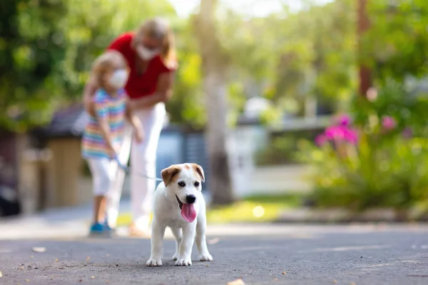 Family walking dog during virus outbreak. Woman and child wearing face mask in coronavirus lockdown and quarantine. Home animal and pet. Mother and child with puppy in pandemic or air pollution.