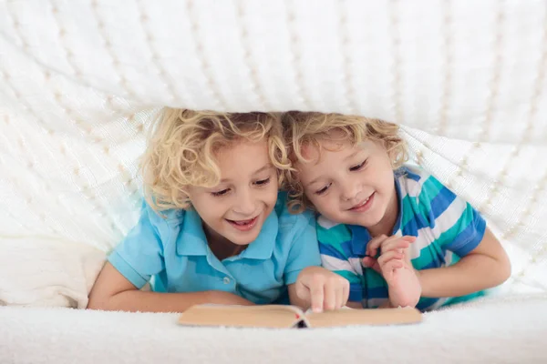 編んだ毛布の下のベッドで子供の読書本 兄弟2人で遊ぶ 子供の居心地の良いベッドルームの巨大なスタイル 寝る前に宿題をする少年 — ストック写真