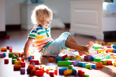 Çocuk renkli oyuncak bloklarıyla oynuyor. Çocuklar oynar. Küçük çocuk güneşli beyaz yatak odasındaki karanlık zeminde oyuncaklardan kule inşa ediyor. Bebek ve bebek için eğitici bir oyun. Çocuklar oyuncak ev yapar.