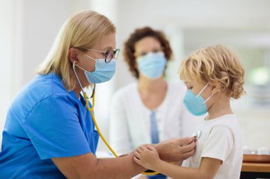 Çocuk doktoru, yüz maskeli hasta çocuğu muayene ediyor. Test ve tarama için sağlık kliniğindeki hasta çocuk. Çocuklar evde virüs tedavisi görüyor. Koronavirüs salgını. Covid-19 salgını. Hasta öksürüyor..