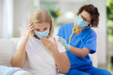 Doktor maske takan hasta hastayı muayene ediyor. Test ve tarama için sağlık kliniğindeki hasta kadın. Evde virüs tedavisi. Koronavirüs salgını. Covid-19 salgını. Kadın öksürüyor, göğsü ağrıyor..