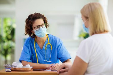 Doktor maske takan hasta hastayı muayene ediyor. Test ve tarama için sağlık kliniğindeki hasta kadın. Evde virüs tedavisi. Koronavirüs salgını. Covid-19 salgını. Kadın öksürüyor, göğsü ağrıyor..