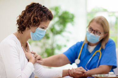 Doktor maske takan hasta hastayı muayene ediyor. Test ve tarama için sağlık kliniğindeki hasta kadın. Evde virüs tedavisi. Koronavirüs salgını. Covid-19 salgını. Kadın öksürüyor, göğsü ağrıyor..