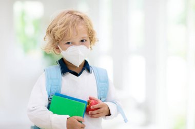 Corona virüsü ve grip salgını sırasında yüz maskesi takan bir çocuk. Çocuklar için hastalık ve hastalık koruması. Koronavirüsü önlemek için cerrahi maskeler. Okul çocuğu öksürüyor. Küçük çocuk okula gidiyor..