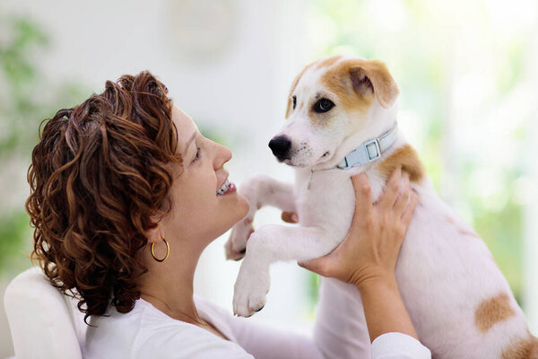 Woman playing with dog. Young woman with curly hair hugging puppy indoors. Family with pet at home. Fun with domestic animal. Love and friendship with pets.