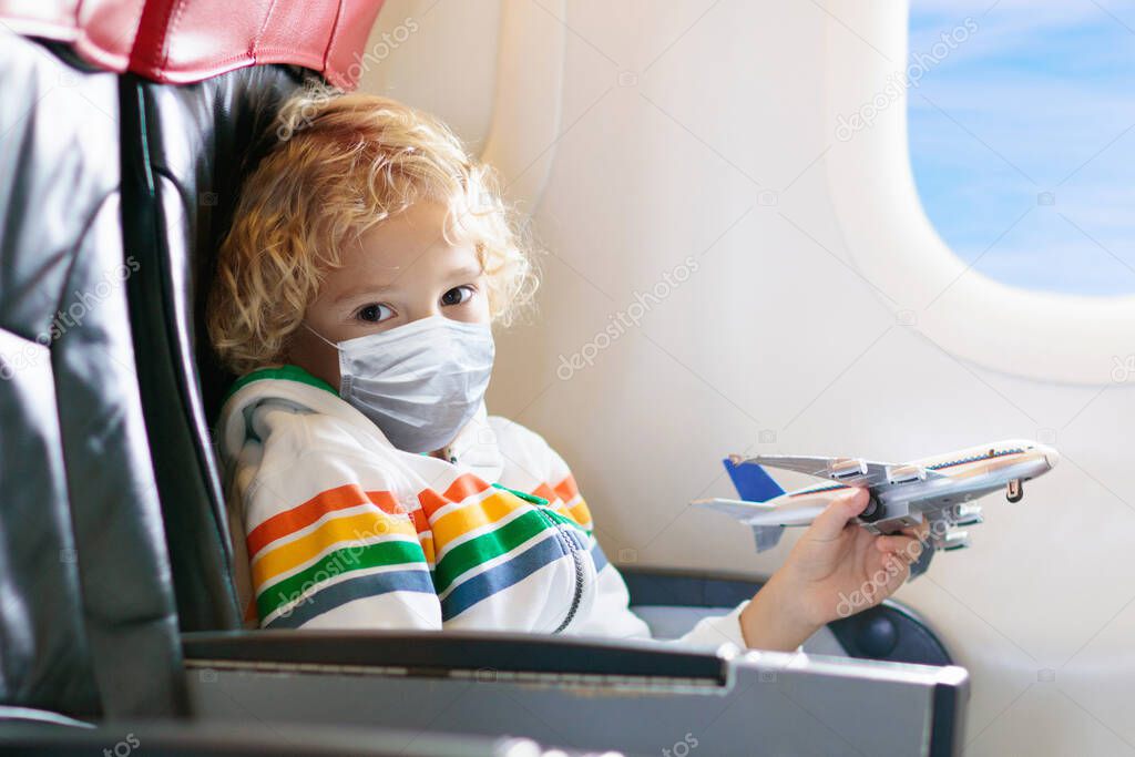 Child in airplane in face mask. Virus outbreak. Coronavirus and flu pandemic. Safe travel with young child and baby. Kids flying airplane in surgical masks.