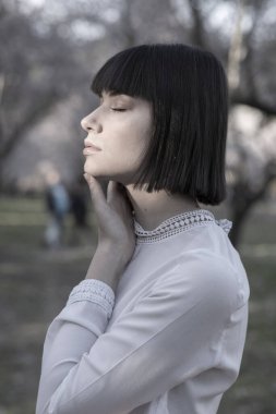 Short black hair model woman, posing in a blooming almond tree field