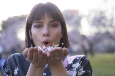 Kısa siyah saçlı kadın model, Japon kimonosuyla çiçek açmış badem ağacı tarlasında poz veriyor.