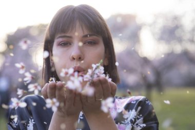 Kısa siyah saçlı kadın model, Japon kimonosuyla çiçek açmış badem ağacı tarlasında poz veriyor.