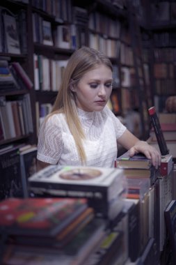 blonde girl with white blouse and black pants climb a ladder in a bookcase