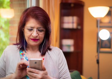 Son sınıf öğrencisi kadın cep telefonu ve kulaklıklarıyla yeni teknoloji aramaları yapıyor.