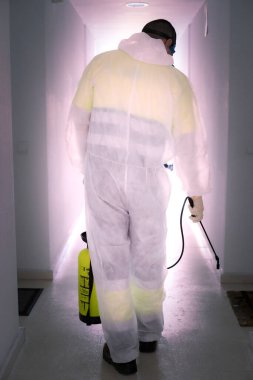 Korunaklı kıyafet giyen bir adam karantina şehrinde salgın olan koronavirüsün yayılmasını önlemek için güneşteki kamusal alanları ilaçlarla dezenfekte ediyor. Covid -19. Temizlik kavramı.