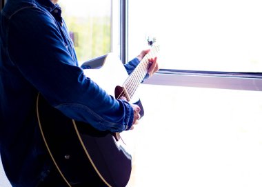 Sakallı şapkalı bir adam yazın balkonda gitar çalar. Yan görüş. Covid - 19