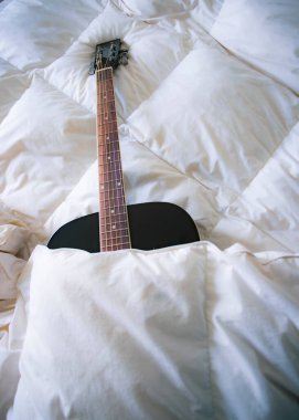 Battaniyeyle kaplı yatakta gitar.