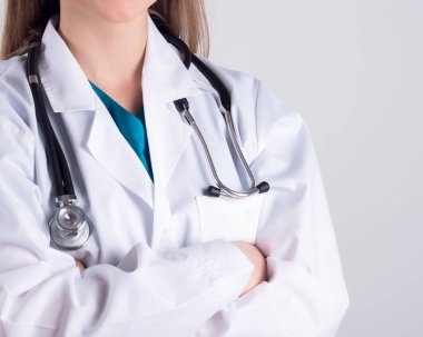 Steteskop kolları katlanmış, beyaz bir arka planda kadın bir doktorun yakın çekimi..