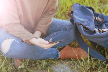 Kadının elleri cep telefonuyla etkileşimde. Sırt çantası var. Doğada bir gezgin.