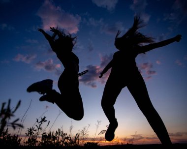 Gün batımında zıplayan iki kız gökyüzü, gölgeler