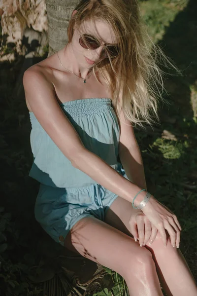 Menina encantadora em um vestido azul, posando sentado à sombra de palmeiras. cabelo acenando ao vento . — Fotografia de Stock