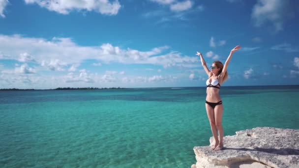 Een meisje staat op een rots tegen het azuurblauwe water van de Caribische zee — Stockvideo