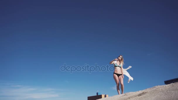 Chica, playa, mar, viento en tu pelo. chica en bikini a color posando a fotógrafo. Su cabello y una capa transparente se desarrollan en el viento . — Vídeo de stock