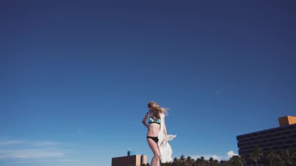 Meisje, strand, zee, wind in je haren. meisje in kleur bikini poseren voor de fotograaf. Haar haren en een transparante cape ontwikkelen in de wind. — Stockvideo