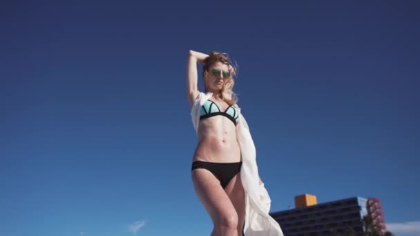 Mädchen, Strand, Meer, Wind im Haar. Mädchen im farbigen Bikini posiert für Fotografen. ihr Haar und ein transparenter Umhang entwickeln sich im Wind. — Stockvideo