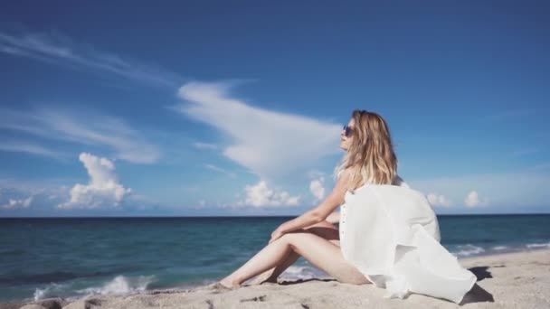 Een meisje zit op het zand en sunbathes. — Stockvideo