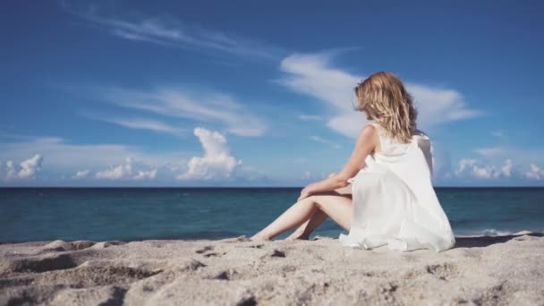 Een meisje zit op het zand en sunbathes. — Stockvideo