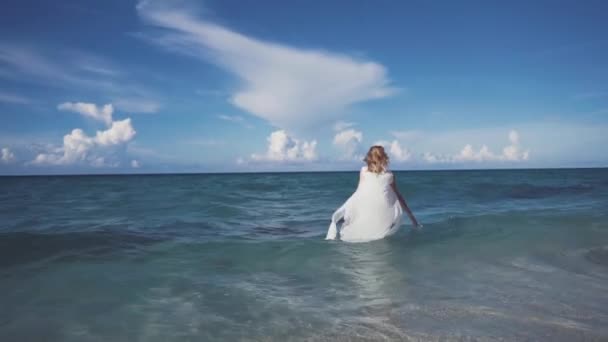 Chica, playa, mar, viento en tu pelo. Hermosa chica sonríe y salpica en las olas del Océano Pacífico. Una túnica de lino se desarrolla en el viento . — Vídeo de stock