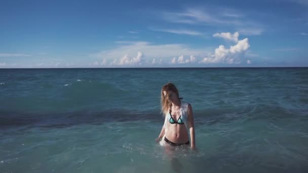 Chica, playa, mar, viento en tu pelo. Hermosa chica sonríe y salpica en las olas del Océano Pacífico. Una túnica de lino se desarrolla en el viento . — Vídeos de Stock