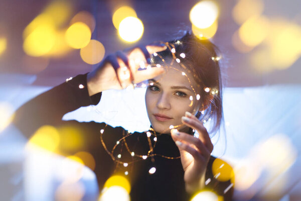 Красивая молодая женщина улыбается и говорит гирлянды огней на городской улице
