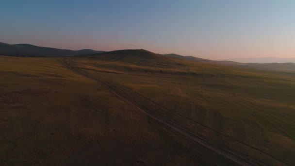 Antenni kenttä kuivaa keltaista ruohoa. Steppe Olkhon Islandilla. Baikaljärvi, Venäjä. Lennokki kukkuloilla auringonlaskussa — kuvapankkivideo