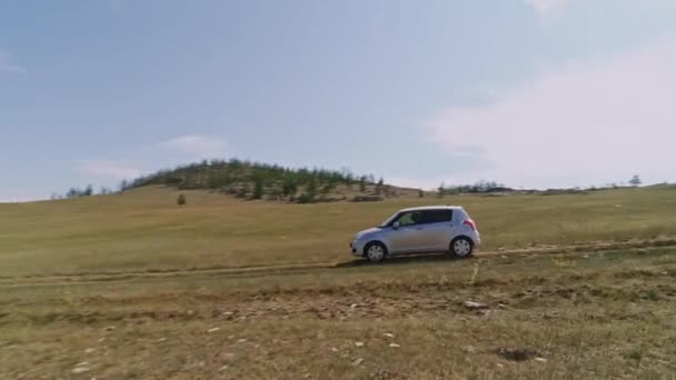 Légi felvétel, amin robogó autó száguld Steppe-ben. Az autó a sztyeppén halad Szibériába, a Bajkál-sziget mentén elterülő utakon, a füves dombokon át.. — Stock videók