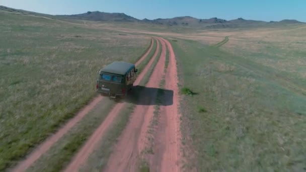 Imágenes aéreas filmadas con un dron de camioneta en la estepa. el coche viaja a lo largo de la estepa a Siberia, caminos establecidos a lo largo de la isla de Baikal a través de las colinas cubiertas de hierba . — Vídeos de Stock