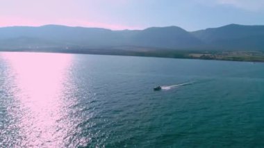 Hava manzaralı uçan drone. Deniz yüzeyinde yüzen küçük bir gemi arkasında köpükten bir su yolu bırakır..