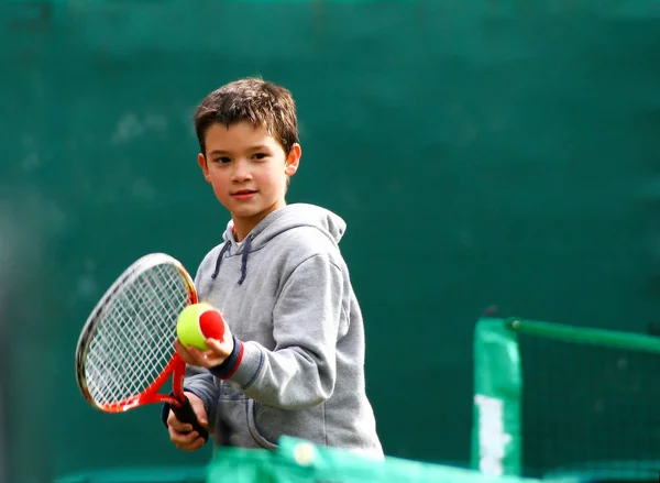 小さな少年学習テニス 緑背景をぼかした写真 — ストック写真