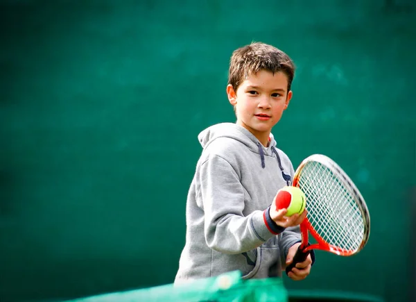 Pequeno jogador de tênis em um fundo verde embaçado . — Fotografia de Stock