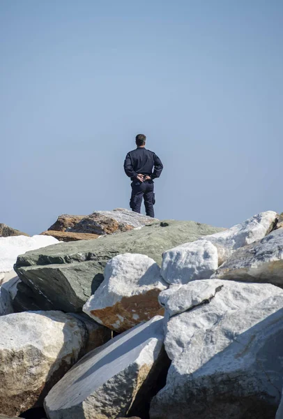 Security man standing alone on big rocks and staring the sea