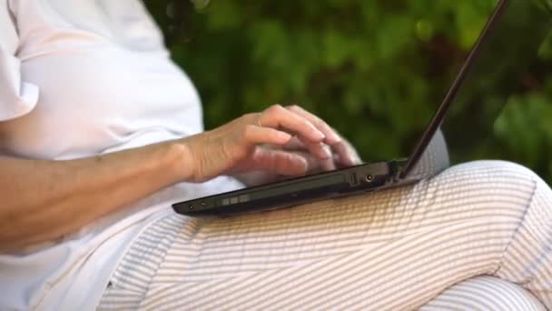 Dorosła kobieta pracująca na zewnątrz na laptopie, uśmiechnięta babcia w średnim wieku pracująca zdalnie na komputerze. — Wideo stockowe