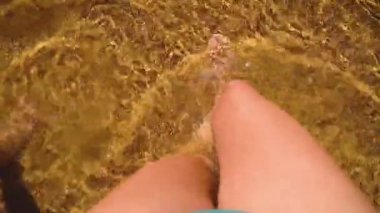 Kristal suyla kumsalda yürüyen bir kadın. Okyanusta deniz dalgaları. Bacak üstü görünümü