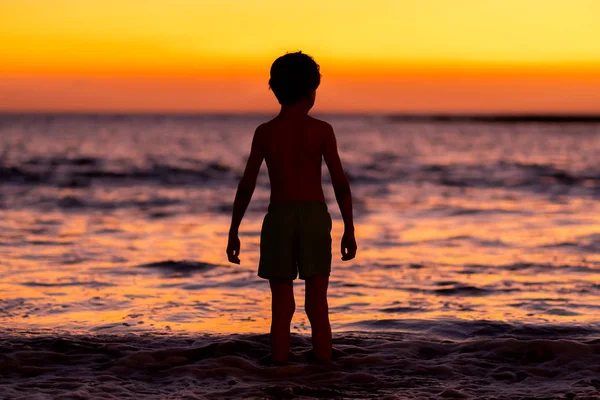 Menino olhando para o pôr do sol no oceano e se preparando para nadar — Fotografia de Stock