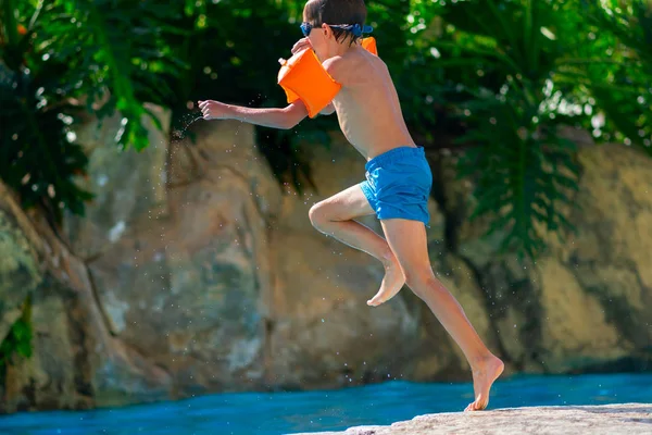 Fiú beleugrik a szabadtéri medencébe. Fiú pihen a nyári üdülőhelyen medencével — Stock Fotó