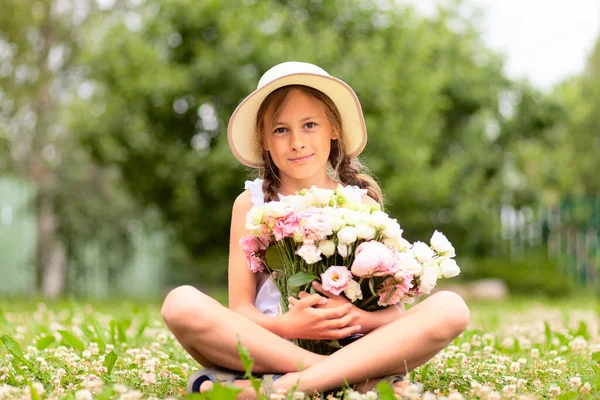 고추가 커다란 꽃다발을 들고 있는 소녀. 챙 이 넓은 모자를 쓰고 꽃피는 초원에 앉아 있는 십 대 청소년. — 스톡 사진