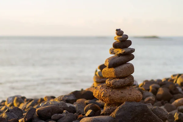 Balanced stone pyramide on shore of the ocean at dawn. Sea pebbles tower closeup symbolizing stability, zen, harmony