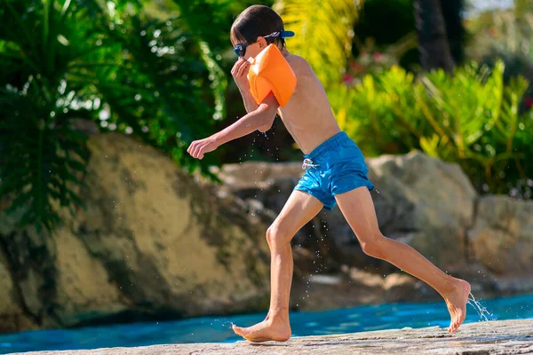 Fiú beleugrik a szabadtéri medencébe. Fiú pihen a nyári üdülőhelyen medencével — Stock Fotó