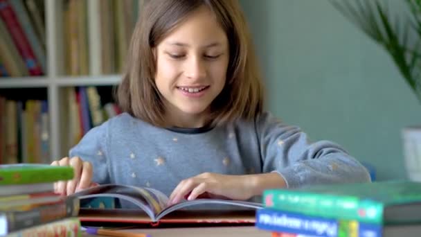 Ein lächelndes Mädchen sitzt an einem Tisch und betrachtet Illustrationen in einem Buch. Nahsicht. — Stockvideo