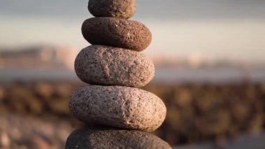 Şafakta okyanusun kıyısında dengelenmiş taş piramit. Deniz çakıl taşları kulesi denge, zen ve uyumu sembolize ediyor.